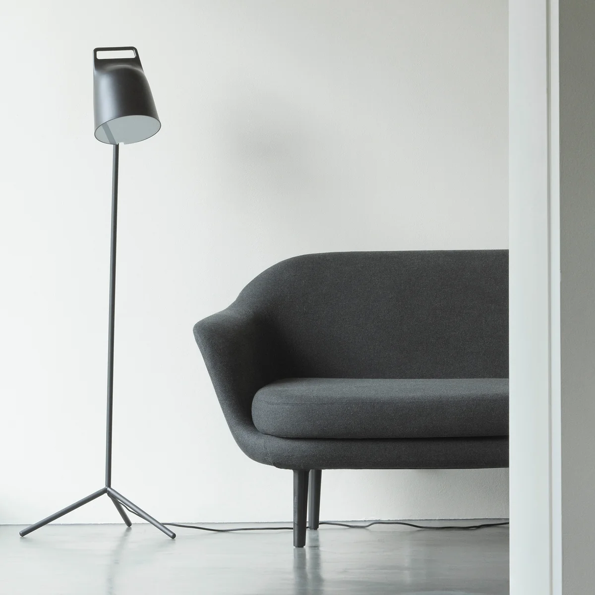 Die Stage LED-Stehleuchte von Normann Copenhagen neben einer grauen Couch