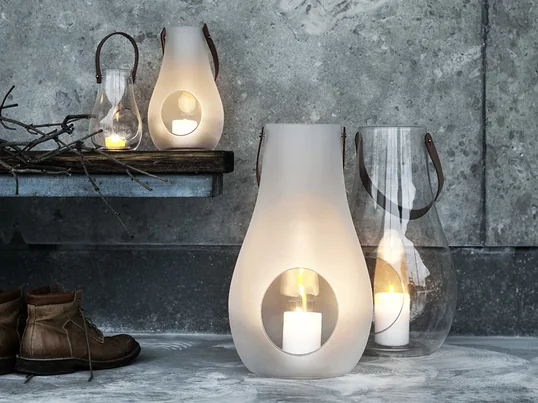 Ein Paradebeispiel für stilvolle und schöne Geschenke für Frauen: die Design with Light Laterne von Holmegaard aus durchsichtigem bzw. matt-weissem Glas und einem Tragegriff aus Leder.