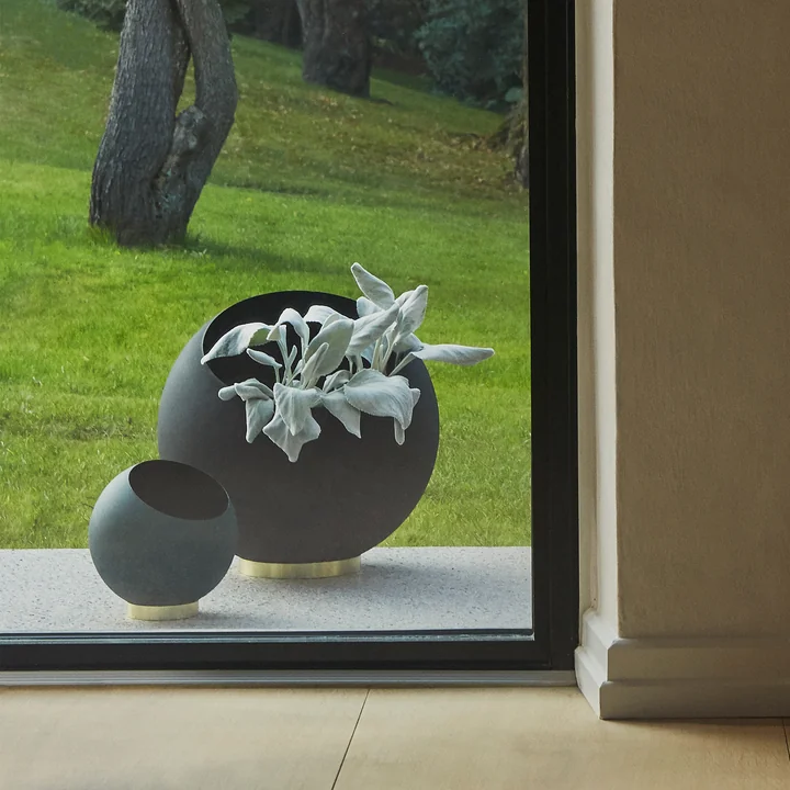 Der Globe Blumentopf von AYTM in seinen verschiedenen Grössen hinter einem bodentiefen Fenster im Freien