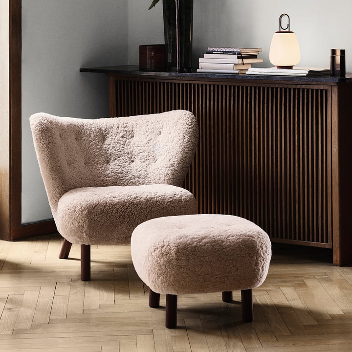 Der Little Petra Lounge Chair mit Pouf von &Tradition vor einer dunkeln Heizkörper-Verkleidung