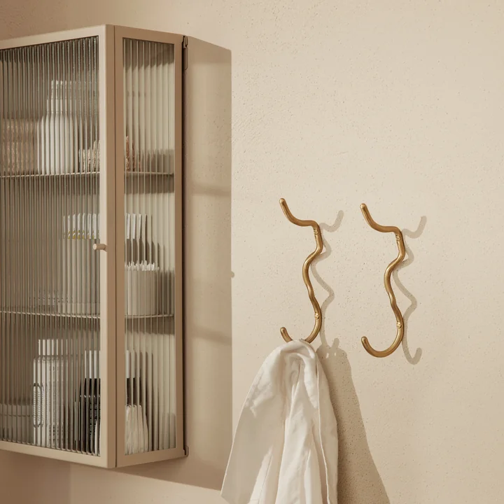 Der Curvature Wandhaken von Ferm Living mit einem Handtuch neben einem Wand-Vitrine