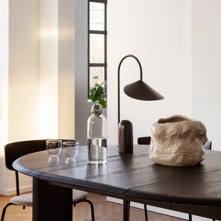 Der Tuck Pflanztopf von Ferm Living auf einem dunklen Holz-Esstisch neben einer schwarzen Tischleuchte