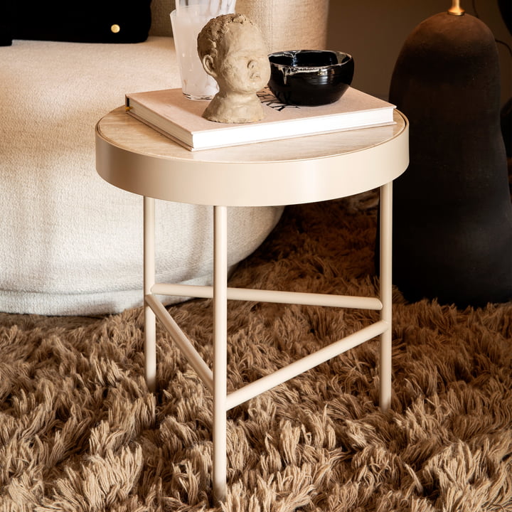 Der kleine Travertine Couchtisch von ferm Living neben einer Couch mit Büchern und Kunstobjekten