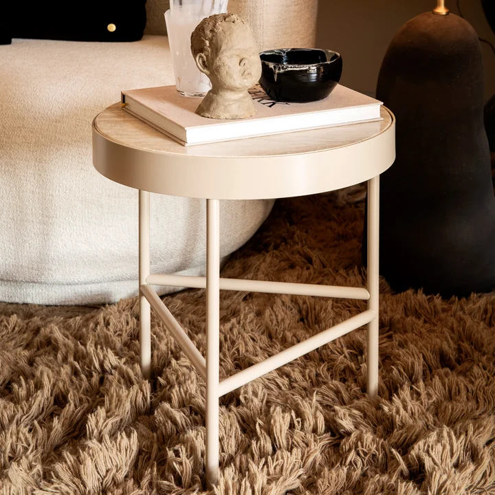 Der kleine Travertine Couchtisch von Ferm Living neben einer Couch mit Büchern und Kunstobjekten