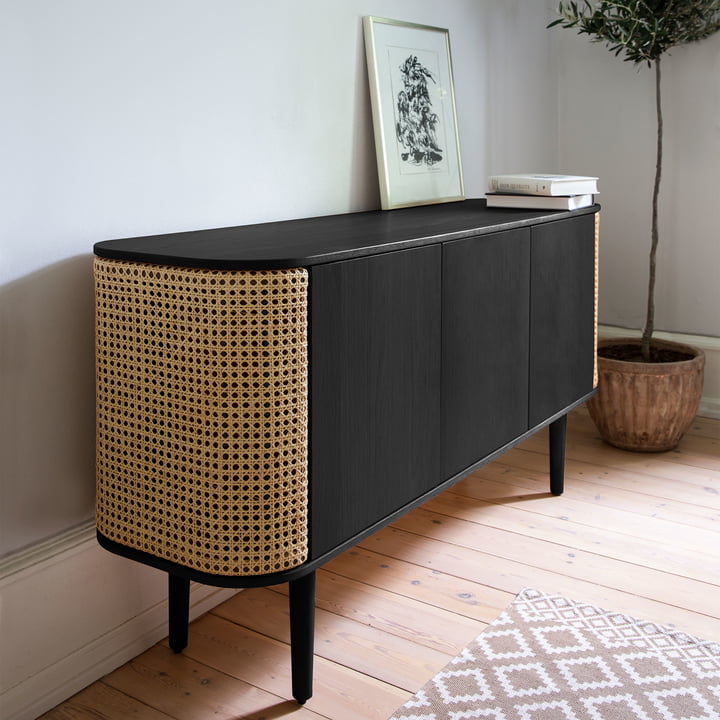 Das Treasures Sideboard von Umage in schwarz / Wiener Geflecht neben einer Zimmerpflanze und Bildern