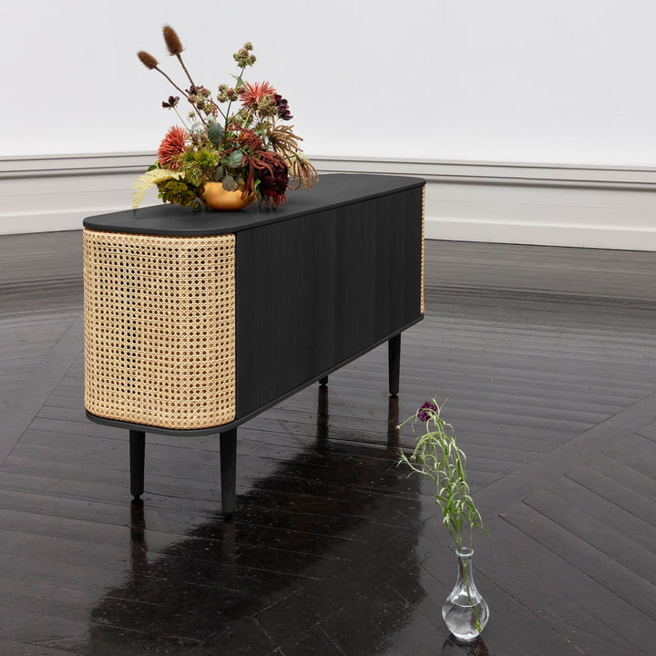 Das Treasures Sideboard von Umage in schwarz / Wiener Geflecht mit Blumen auf einem schwarzen Parkettboden