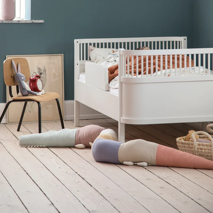 Das verspielte Sleepy Croc Kissen von Sebra neben dem weissen Kinderbett